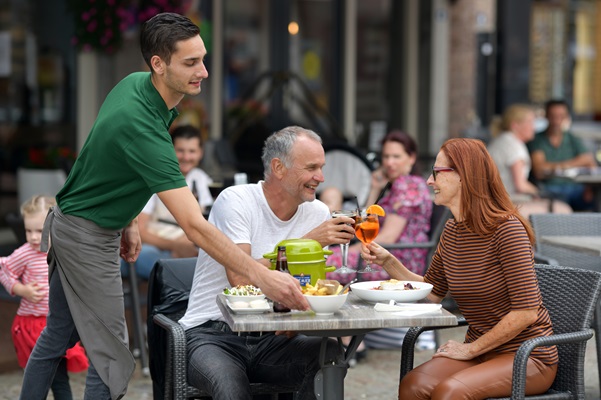 Waiter brings lunch to table where elderly man and woman are toasting