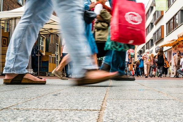 Drukke winkelstraat tijdens koopzondag in Weert. Op de voorgrond lopen mensen voorbij, met focus op hun voeten en tassen. Op de achtergrond zijn winkelende mensen, marktkramen en winkels te zien.