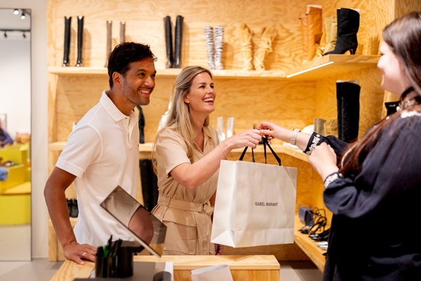Een stel krijgt een winkeltas aangereikt van een verkoopster in een schoenenwinkel in het Designer Outlet Roermond.